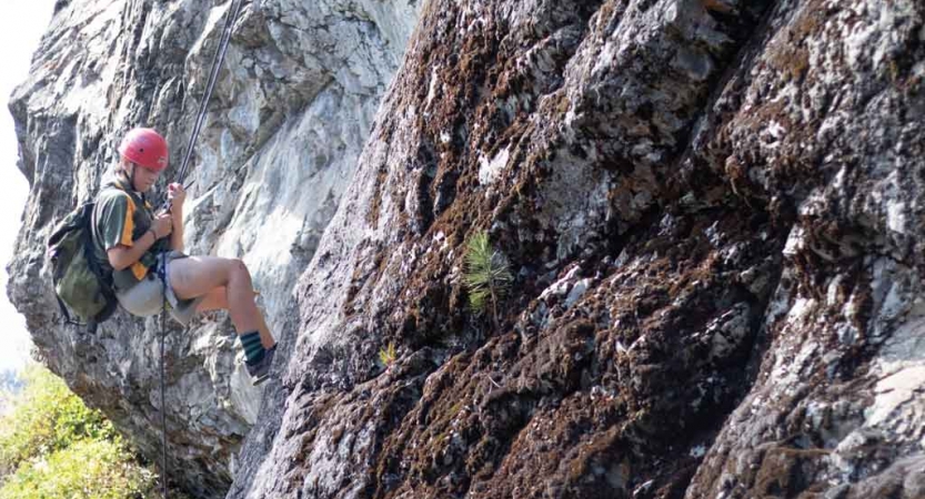 a person looks down as they take a break from rock climbing on an outward bound course